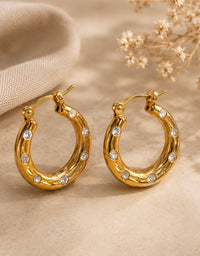 Pair of gold hoop earrings with ripple texture and cubic zirconia stones on a flat surface