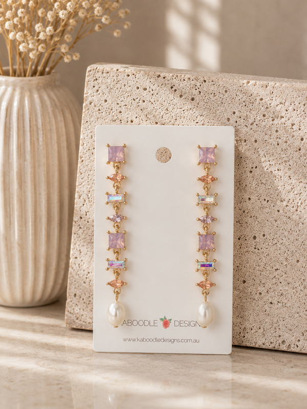 Long rhinestone drop earrings on card, showing pink, iridescent and gold gems ending in a pearl