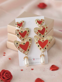 Gold-tone triple heart drop earrings with red enamel, rhinestones and faux pearl, shown on card