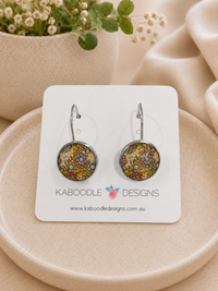 Round floral dangle earrings on card with busy pink, yellow and teal pattern under glossy resin