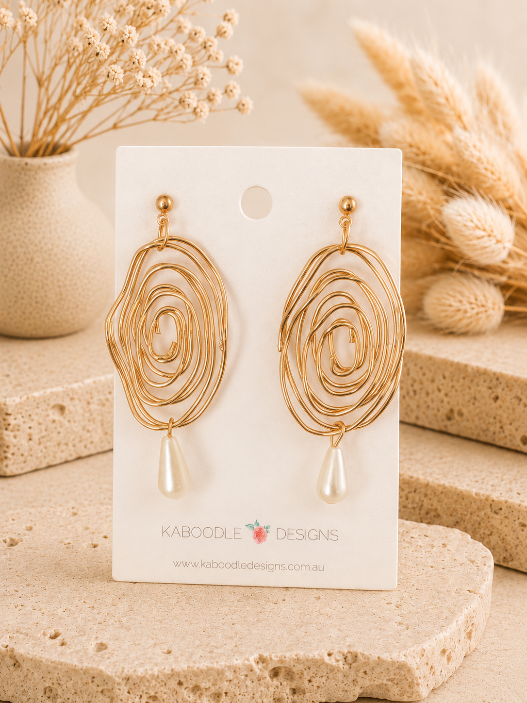 Pair of gold-tone spiral swirl earrings with faux pearl drops displayed on a card