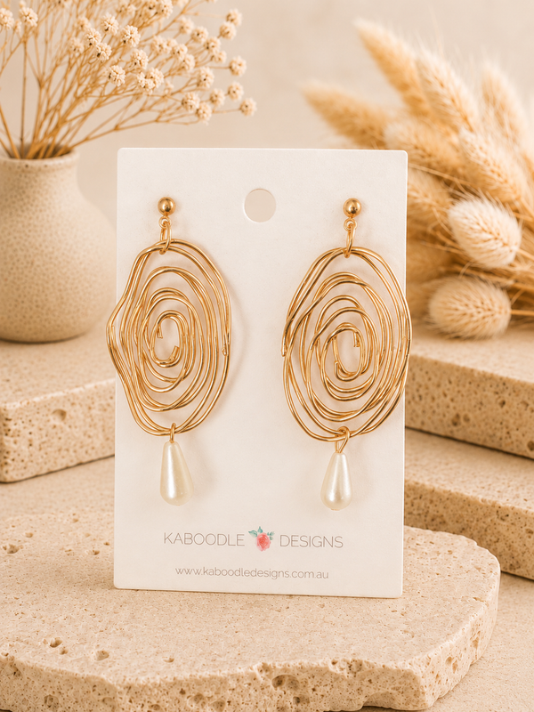 Pair of gold-tone spiral swirl earrings with faux pearl drops displayed on a card