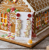 Gingerbread man earrings displayed on card in front of a gingerbread house with candy details