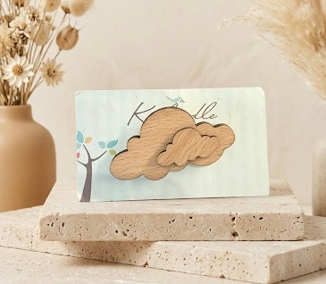 Cloud-shaped wooden brooch with natural wood grain finish, displayed on a branded card