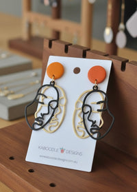Face outline drop earrings with orange stud top on white display card