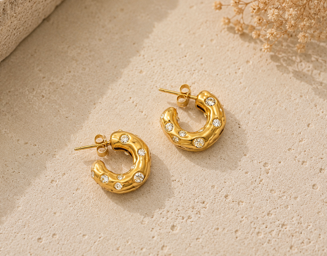 Two gold hoop earrings with textured band and scattered cubic zirconia studs on stone surface
