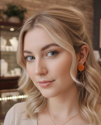 Close-up of model wearing orange stud and black face outline earring
