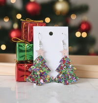 Glitter acrylic Christmas tree drop earrings with star topper on display card, gift boxes and tree in background