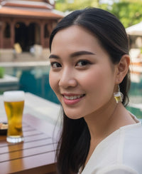 Close-up of woman wearing a beer mug drop earring with a full beer glass on the table beside her