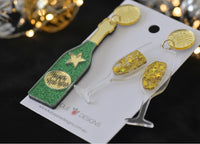 Close-up angled view of champagne earrings showing glitter bottle detail and gold star-filled glasses