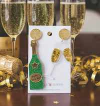 Green glitter champagne bottle and gold confetti-filled champagne glass earrings on card with gold firework studs