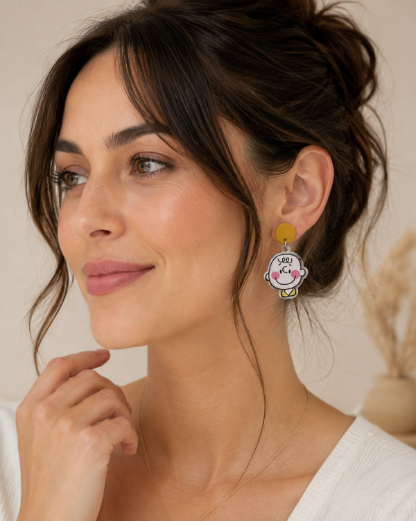 Close-up of a woman wearing a mustard stud and cartoon boy face drop earring
