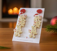 Close-up of stacked gingerbread earrings on card with fireplace and bauble in background
