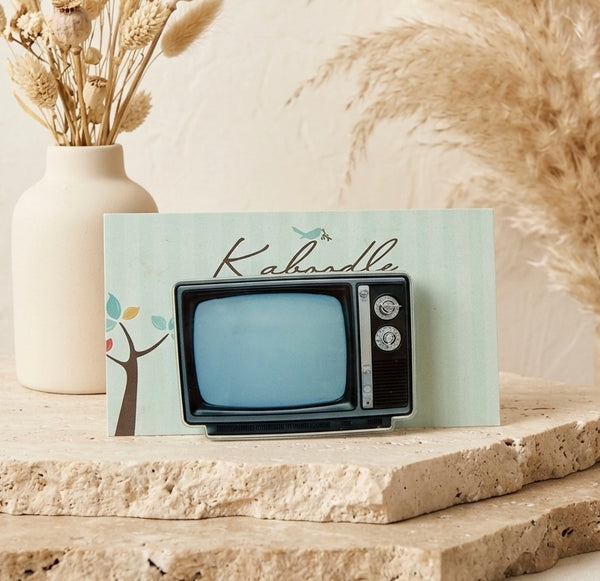 Retro-style television brooch shaped like an old box TV set with black frame, blue screen and side dials
