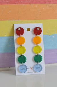 Rainbow acrylic circle drop earrings on white card against striped pastel background