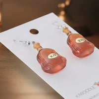 Close-up of XO bottle earrings on card showing cork top, rounded shape and mini label detail