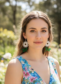 Model wearing white daisy and green leaf drop earrings outdoors