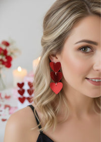 Close-up of red heart drop earrings worn on a model's ear, cascading past her hair