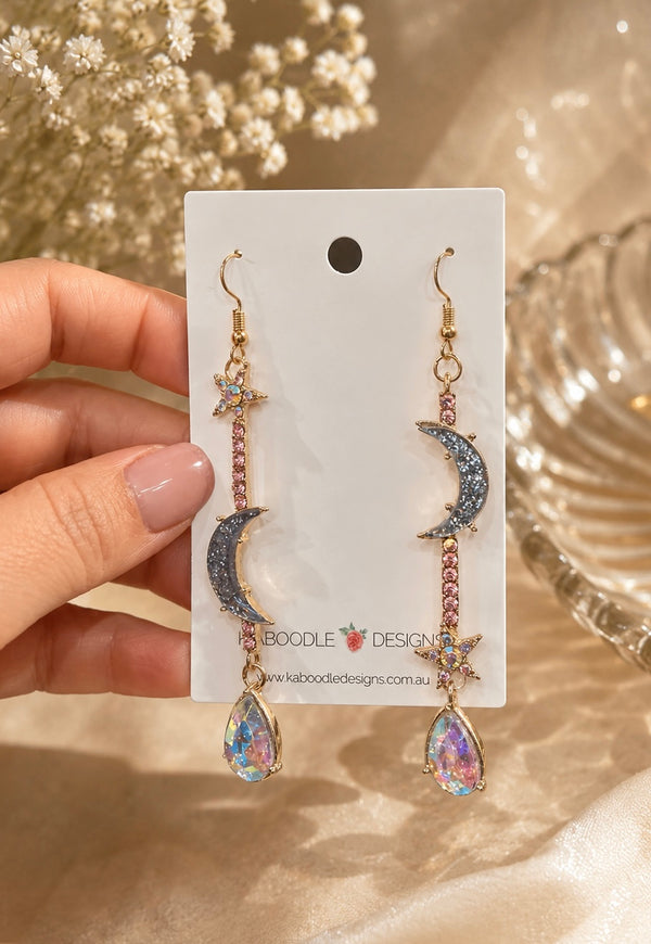 Celestial drop earrings on card featuring crescent moon, star and iridescent teardrop, held in hand