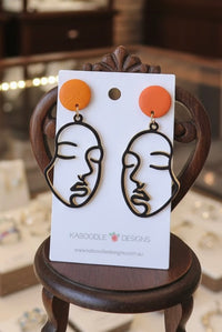 Pair of abstract face line drop earrings on white card, front view