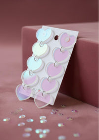 Angled view of translucent heart earrings on card against pink backdrop