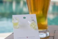 Pair of beer mug earrings on display card, angled view with beer glass in background