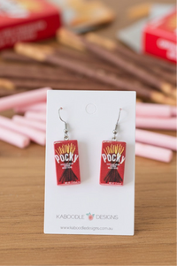 Red Pocky box resin drop earrings on a white display card with real Pocky sticks blurred behind
