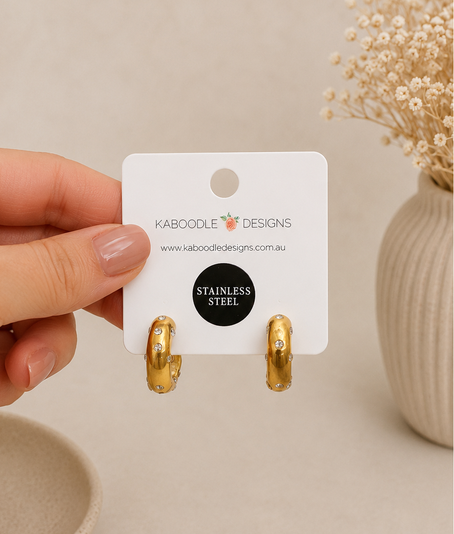 Gold hoop earrings displayed on Kaboodle Designs branded card, held in hand