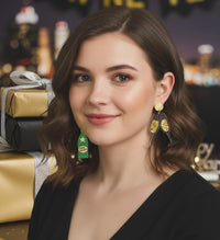 Model wearing green champagne bottle and gold glass New Year earrings against a city skyline backdrop