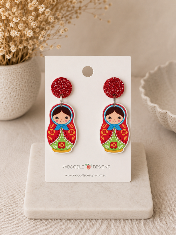 Pair of babushka doll dangle earrings with red glitter stud tops, shown on a display card