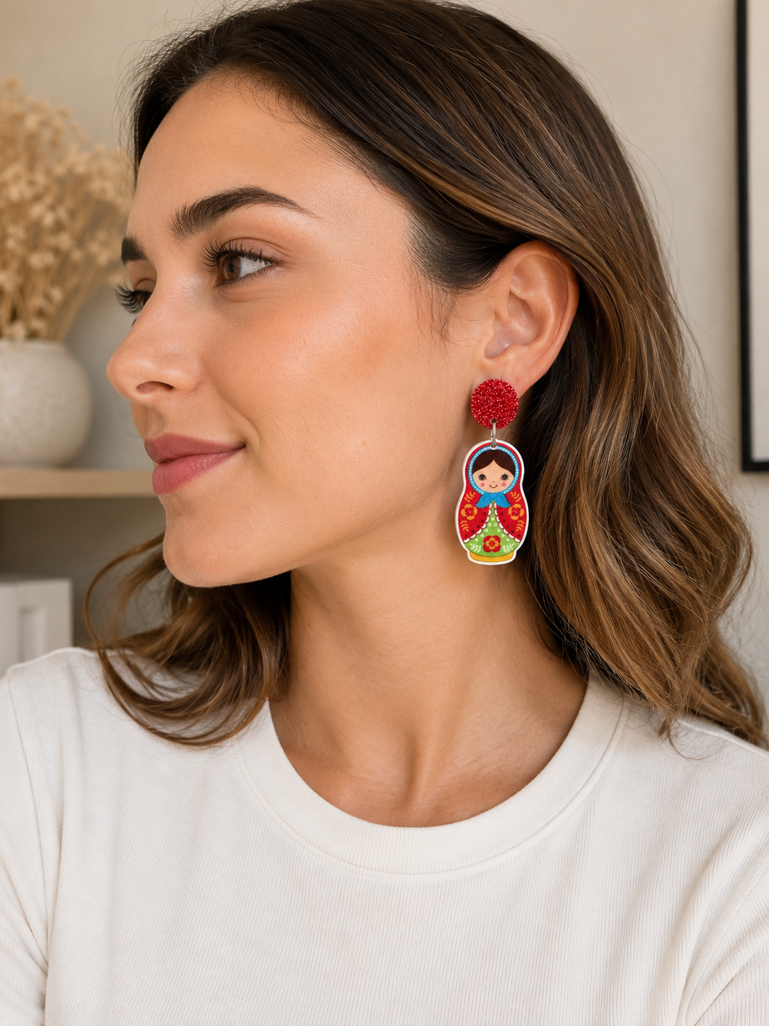 Close-up of a woman wearing a red glitter stud and babushka doll dangle earring