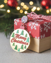 Single gold bauble drop earring with confetti stud resting beside a wrapped gift box with fairy lights behind