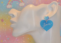 Close-up side view of blue heart earring with 'Lover' text worn on model's ear