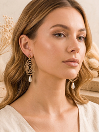 Close-up of model wearing gold spiral swirl earrings with faux pearl drops