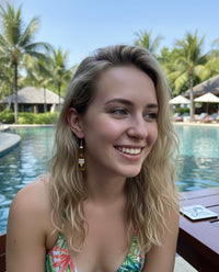 Woman wearing a resin beer bottle drop earring, side profile view by a pool