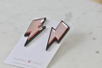 Close-up angled view of lightning bolt earrings showing glossy mirror finish and black edge