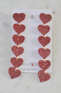 Six red glitter acrylic hearts linked in a cascading drop earring on white card