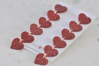 Angled close-up of red glitter heart earrings showing sparkle and gold link detail