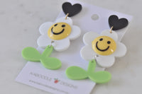 Close-up of daisy smiley face earrings showing yellow face, white petals and green leaf detail
