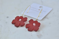 Red poppy earrings lying flat beside their branded backing card, showing glossy finish