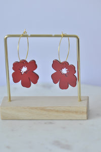 Pair of red poppy drop earrings hanging on a gold display stand against grey background