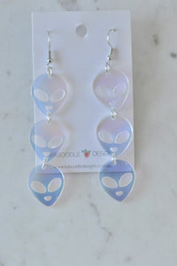 Pair of translucent acrylic alien head drop earrings with three tiers each, shown on card