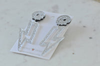 Silver glitter skull and lightning bolt earrings laid flat, angled view showing sparkle