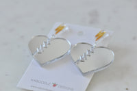 Pair of cracked mirror heart earrings with gold lightning bolts laid on card, angled view