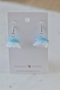 Blue and white resin jellyfish dangle earrings displayed on a card