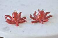 Two red octopus earrings laid flat, showing glossy finish and black bead eyes