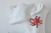 Close-up of red octopus earring worn on ear, showing tentacle detail