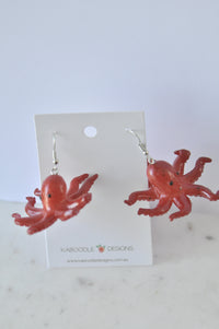 Pair of red plastic octopus dangle earrings on Kaboodle Designs card, front view