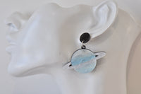 Close-up of blue Saturn earring worn on ear showing glitter and ring detail
