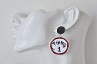 Close-up side view of Thing 1 earring worn on ear, showing red and black circle design